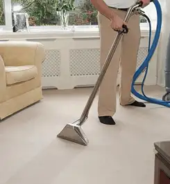 Professional carpet cleaner using a hot-water extraction wand and hose machine in a living room in Manchester, NH.