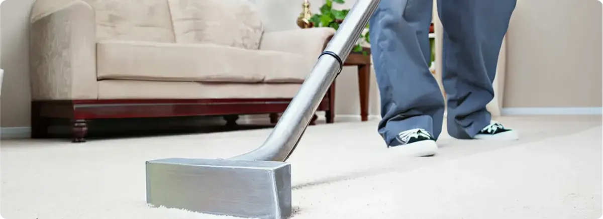 Carpet cleaning technician using a hot-water extraction wand on a light-colored carpet in a living room, Manchester, NH.